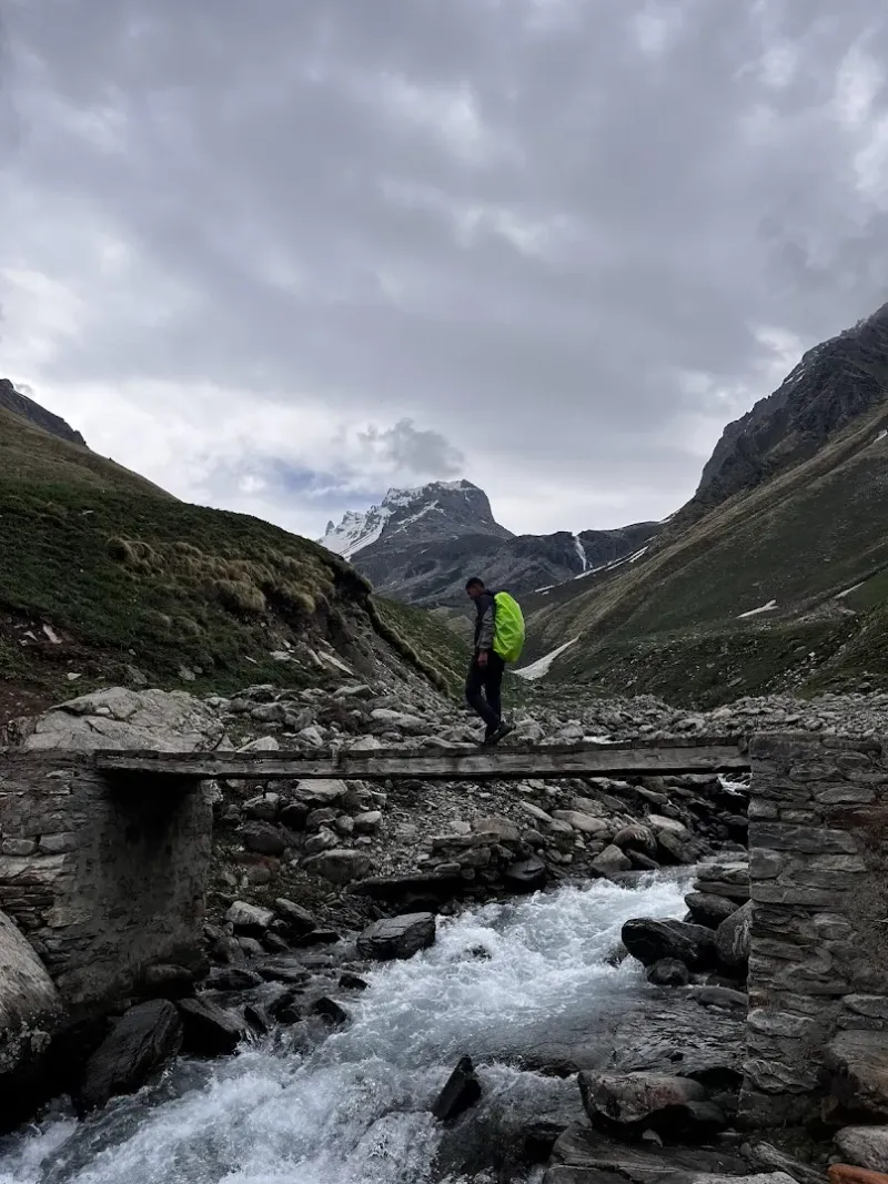 Crossing over to the north wall — the rustic wooden bridge leading us toward our high base. Chandranahan high pass in background. | © MountRoutes